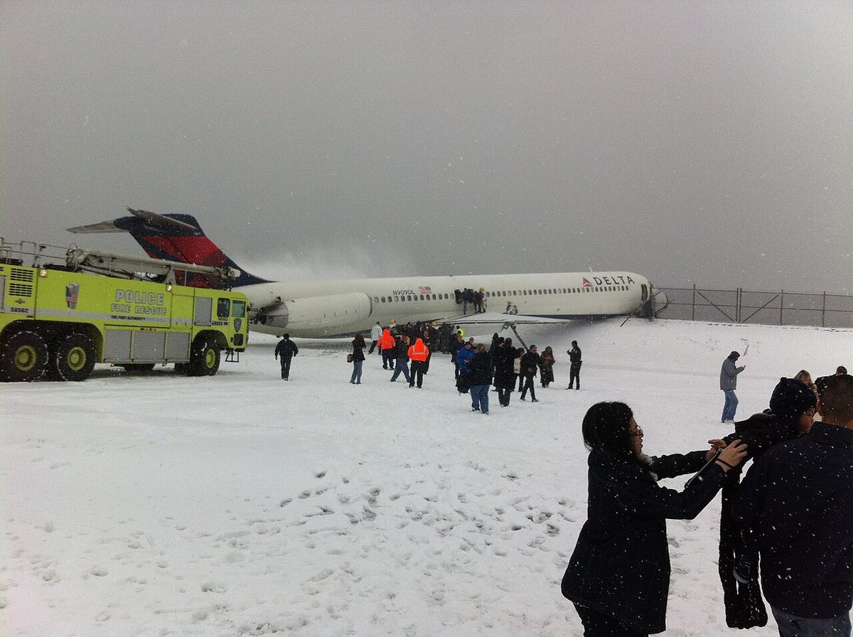 The Delta Air Lines MD-88 of flight 1086 at rest in the snow after leaving the runway at LaGuardia on 5 March 2015, with fire vehicles alongside.