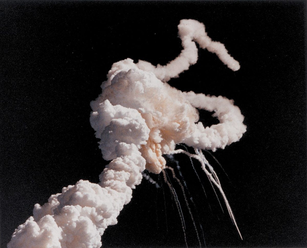 A large white cloud of vapour in a blue sky with smoke plumes twisting away from it, seconds after the break-up of the Space Shuttle Challenger.