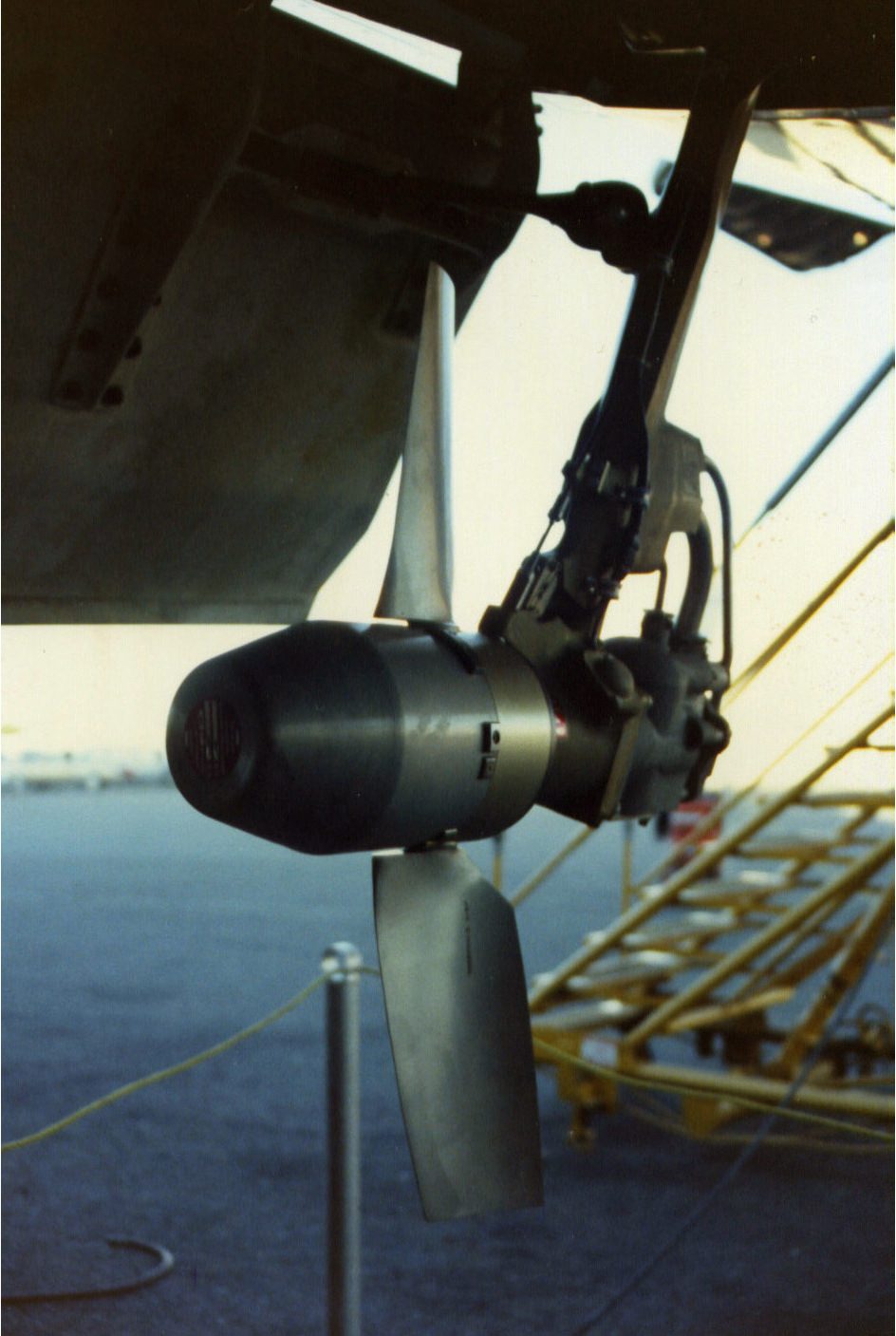 A small two-bladed turbine on a strut hanging below the belly of an airliner, with a set of steps behind it.