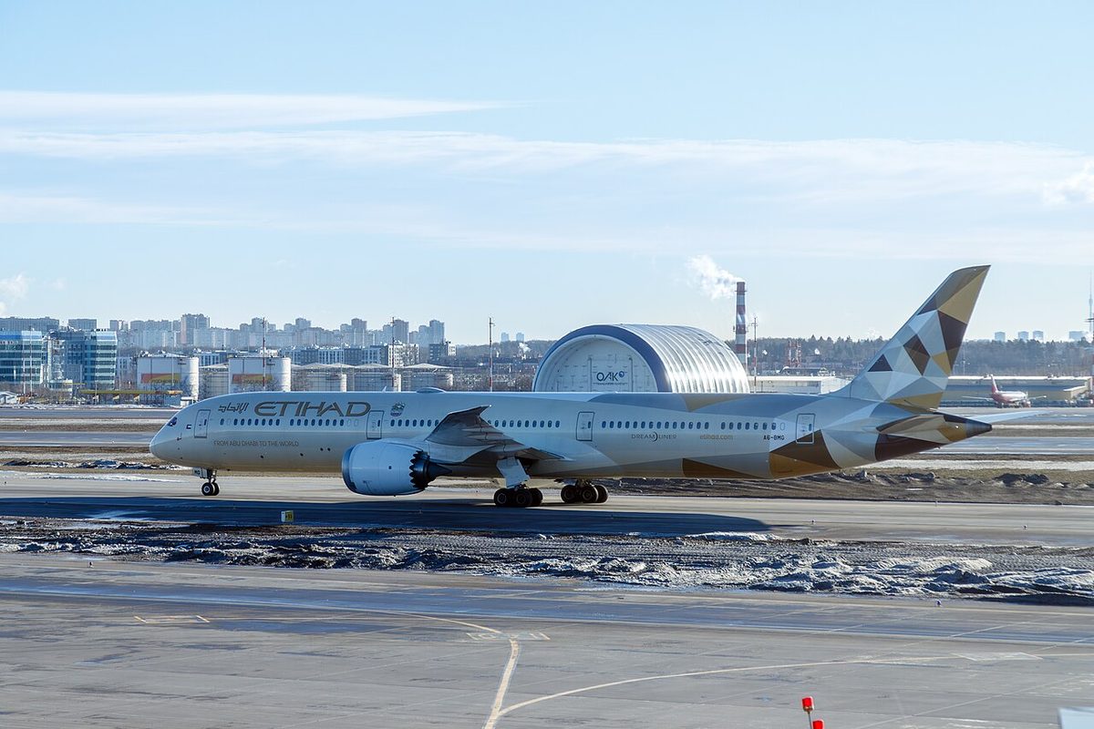 An Etihad Boeing 787-10 taxiing on a snowy apron, seen from the side, its long fuselage filling the frame.