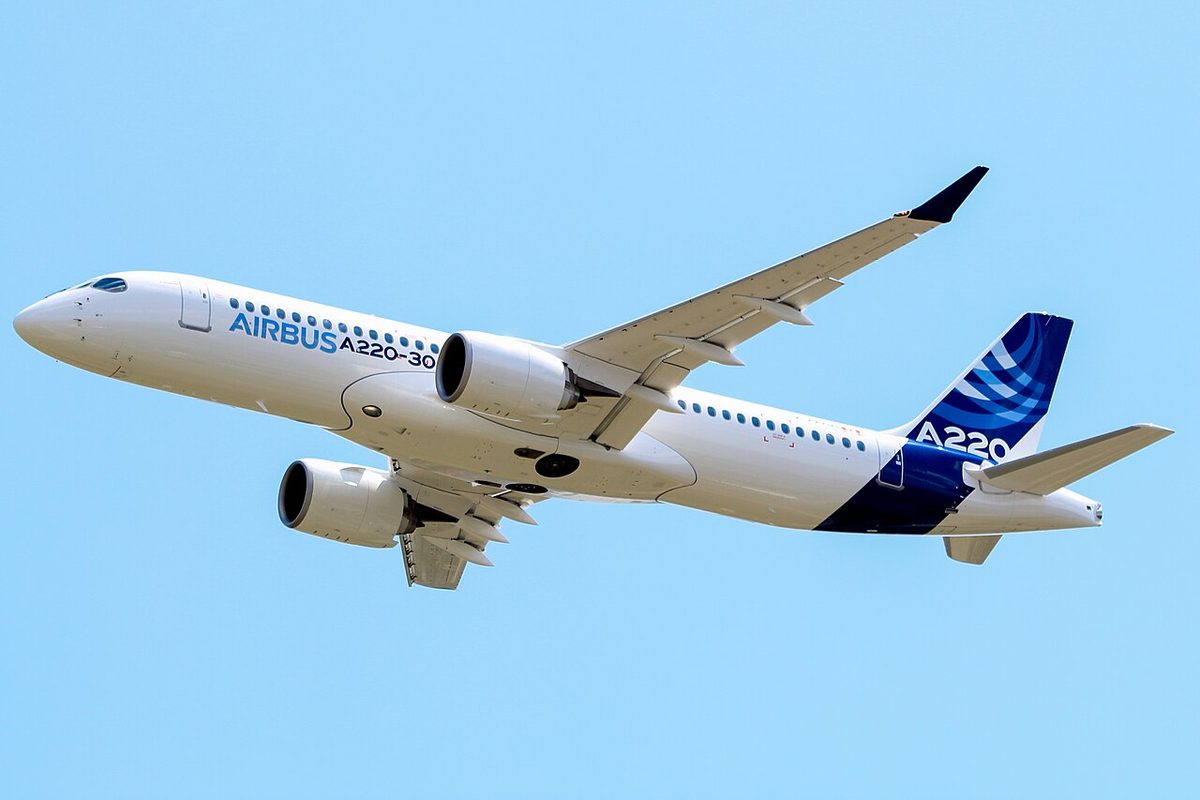 A twin-engine airliner in Airbus house colours seen from below on a low pass, 'AIRBUS A220-300' on the forward fuselage and 'A220' on the fin.