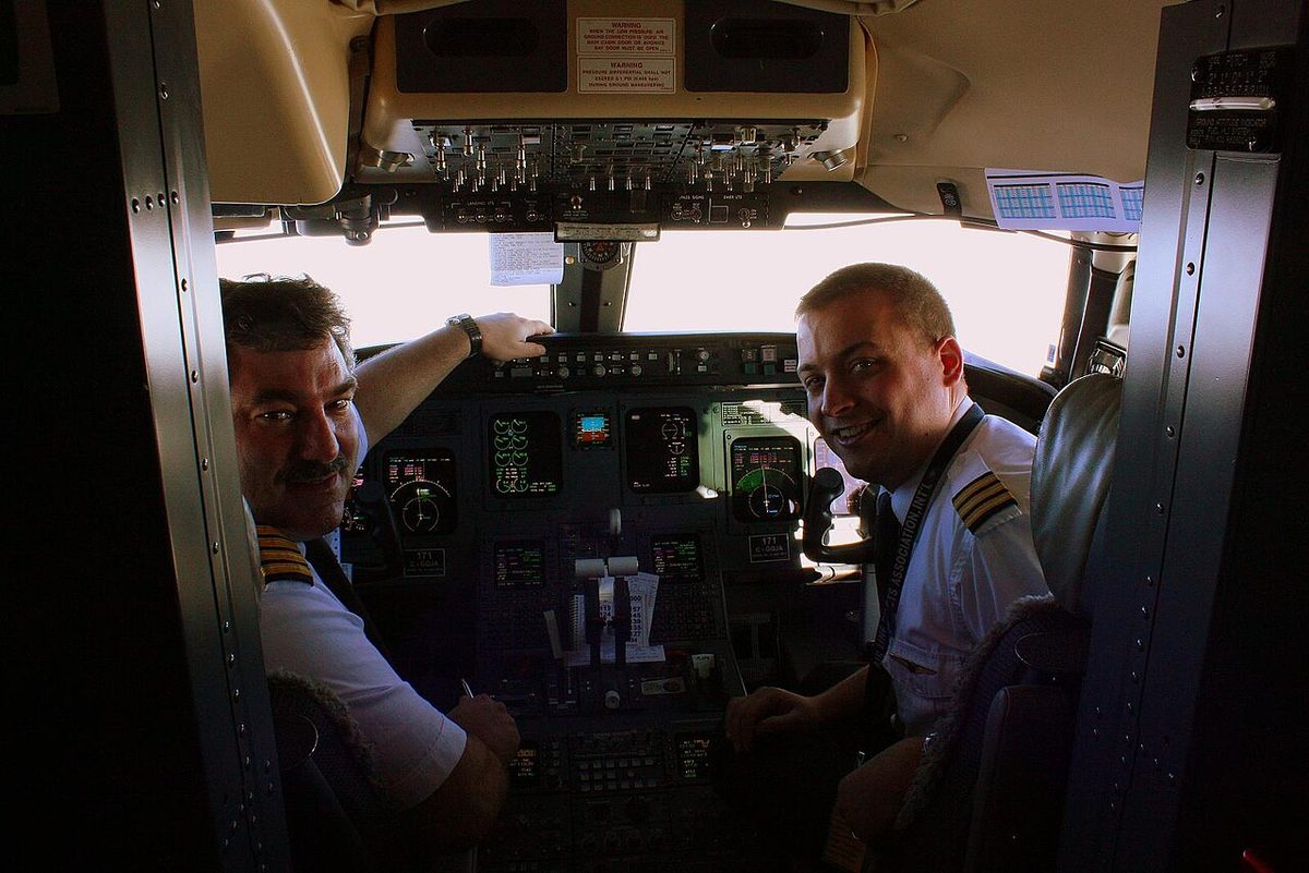 Two pilots in white uniform shirts seated side by side at the controls of an airliner, turned towards the camera.