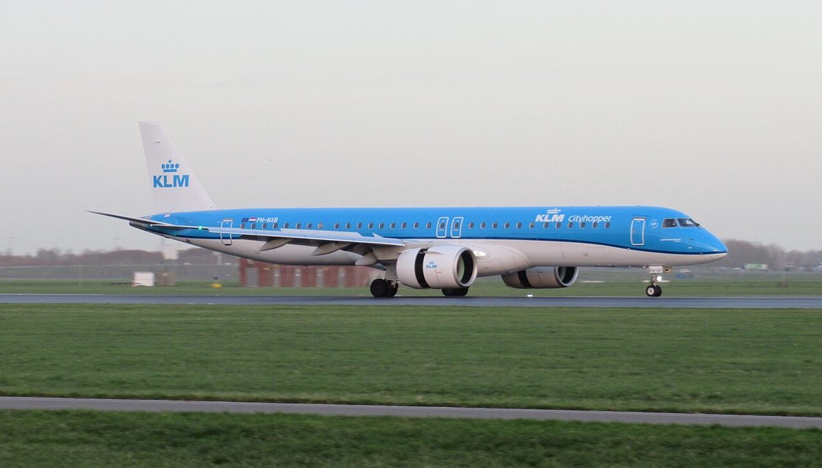 A light blue twin-engined airliner rolling along a runway, seen from the left, with two exit outlines on the fuselage above the wing.