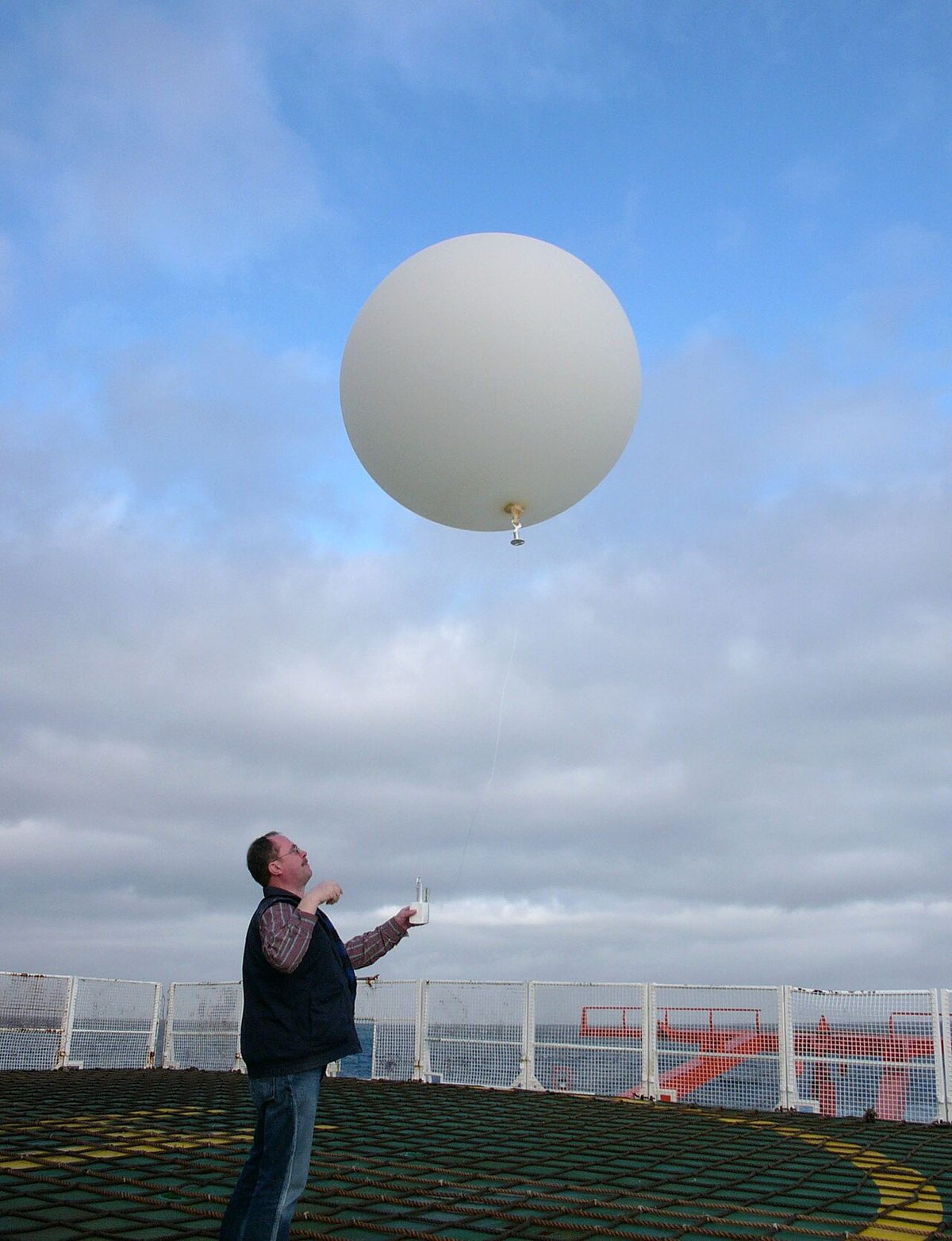 A person on a ship's deck releasing a large white weather balloon with a small instrument package on a line below it.