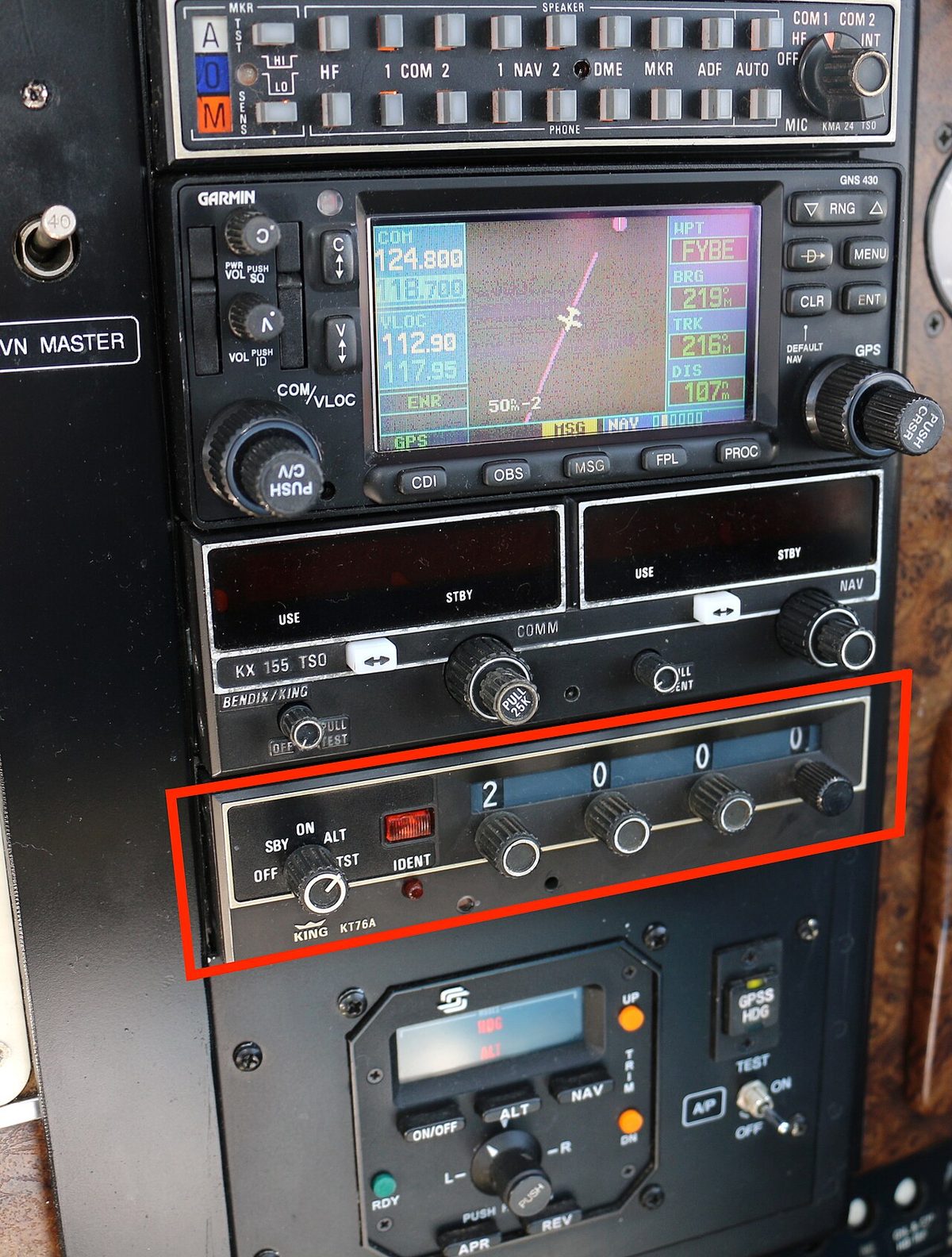 Avionics stack in a light aircraft: a radio with active and standby frequency windows above a transponder, outlined in red, whose four code knobs are set to 2000.