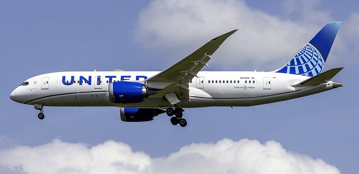 A United Airlines Boeing 787-8 on final approach, landing gear down, seen from the side against a blue sky.