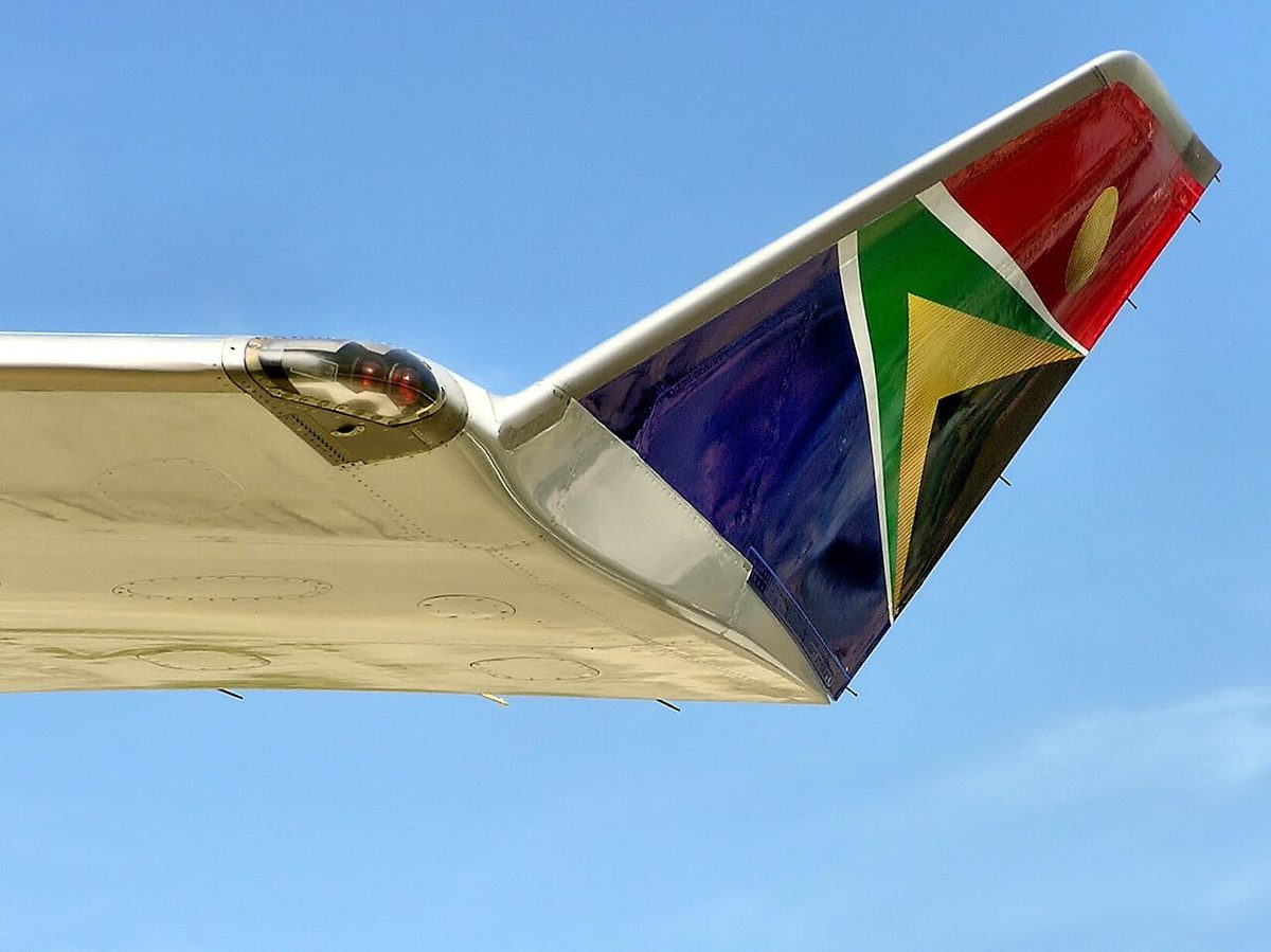An airliner's wingtip curving up into a winglet painted in national flag colours, with a navigation light housing at the base of the winglet.