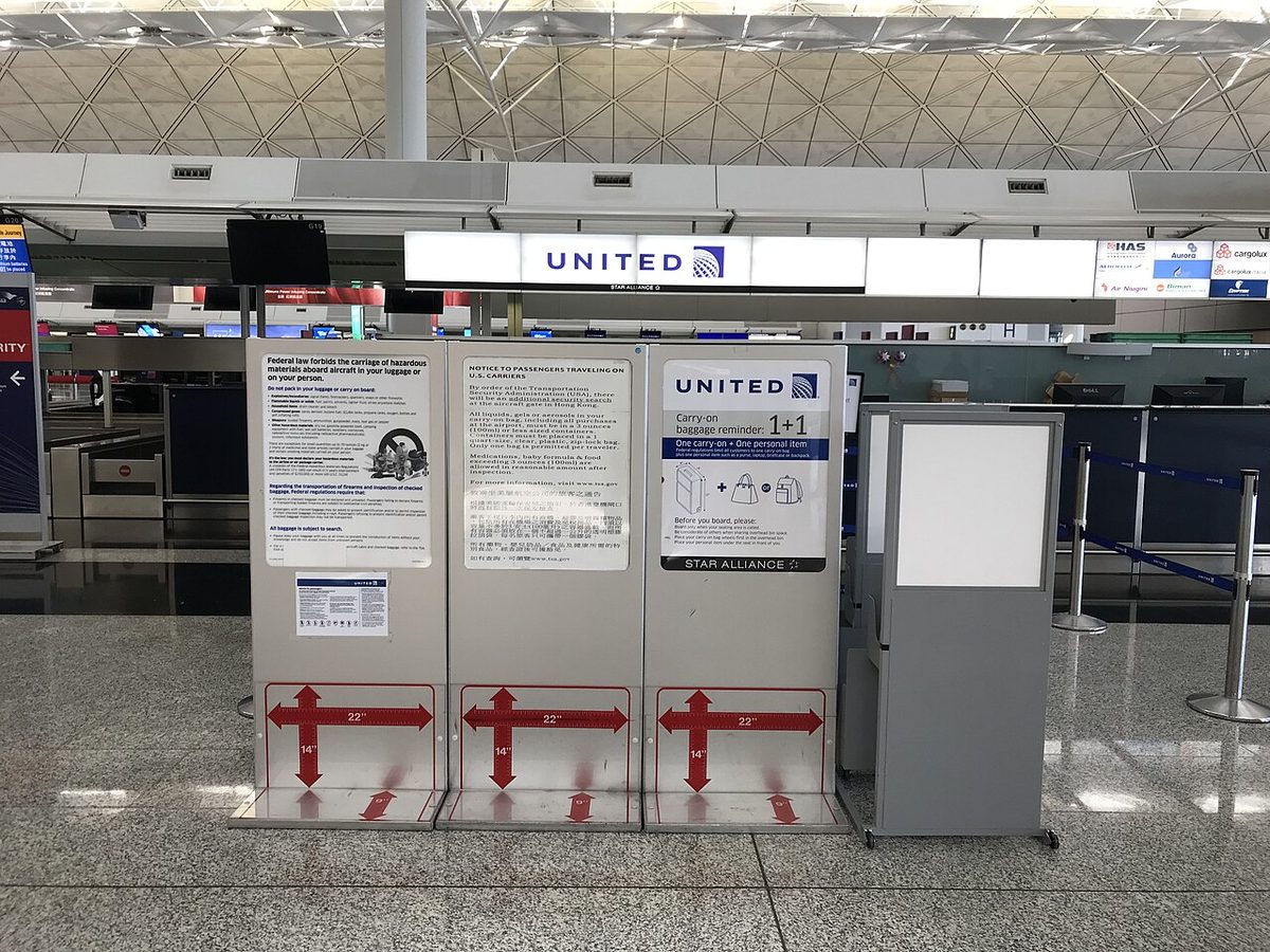 Three carry-on bag sizers with size markings and notices on hazardous materials and the carry-on allowance, in front of United Airlines check-in desks in Hong Kong.