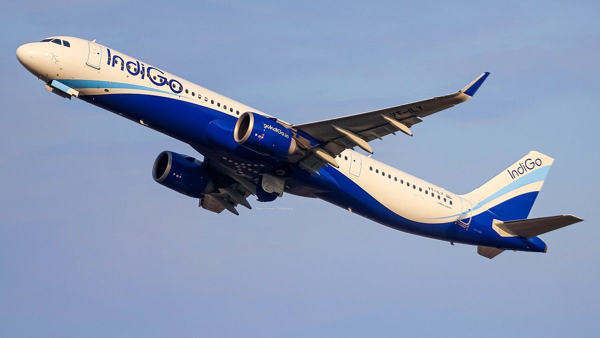 A white and dark blue IndiGo Airbus A321neo climbing against a pale blue sky.