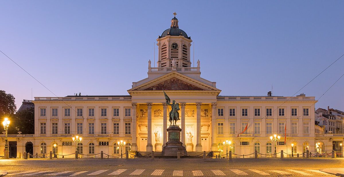 A floodlit neoclassical church with a domed bell tower and an equestrian statue in front, under an even blue and violet twilight sky.