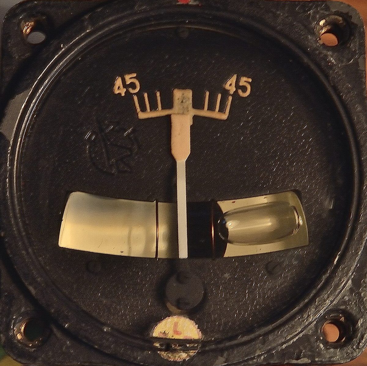 Round instrument with a vertical white needle over a row of marks and a curved glass tube for the slip ball below it.