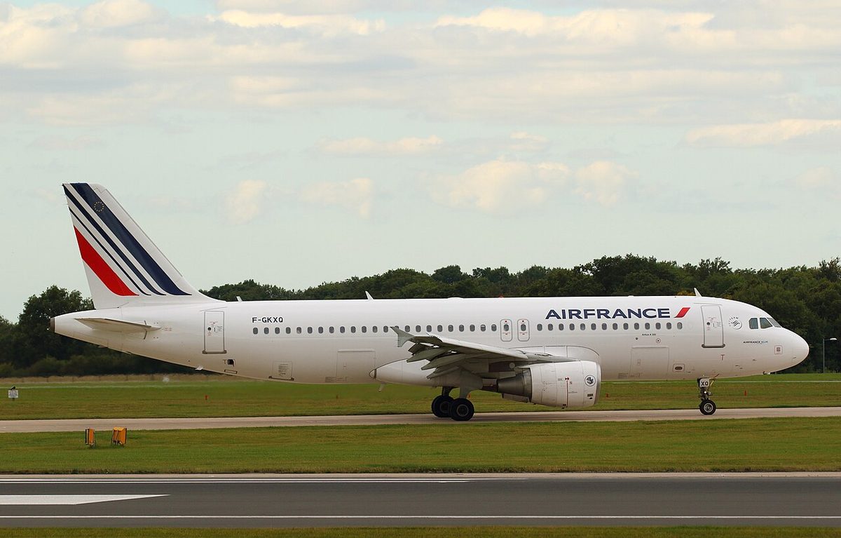 A white Air France Airbus A320 with a blue, white and red striped tail on a runway, trees behind.
