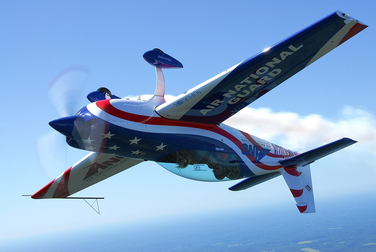 A single-engine aerobatic monoplane flying inverted against a blue sky.