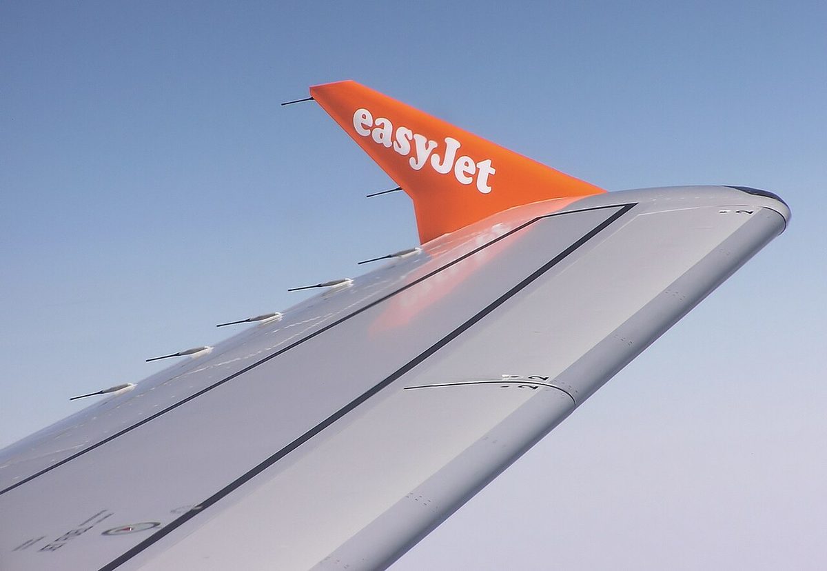 An airliner wing tip and orange winglet seen from the cabin, with a row of thin rods sticking out behind the trailing edges.