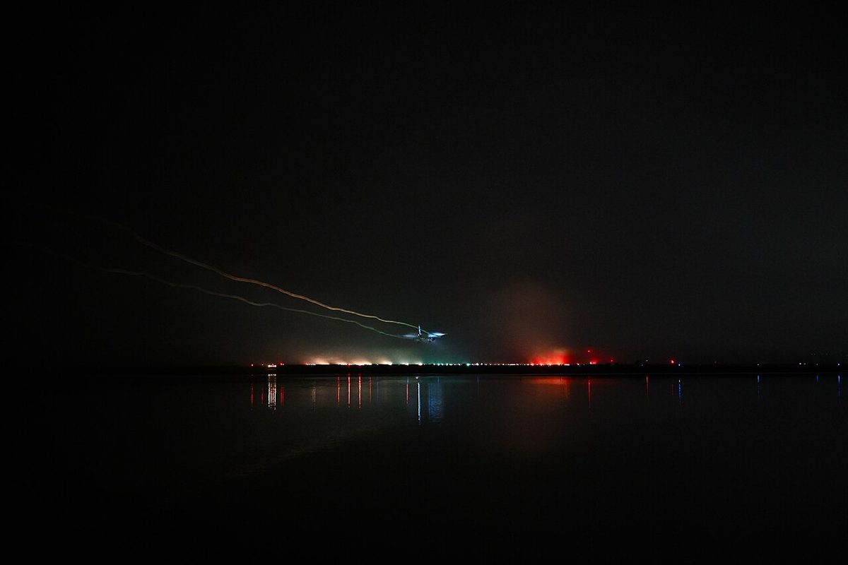 A night long exposure of an airliner's lights streaking low over airport lights glowing in fog.