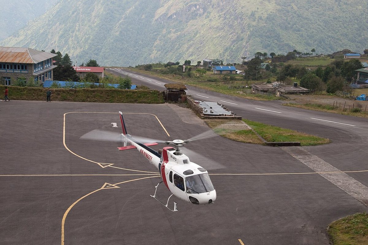 A helicopter on the apron at Tenzing-Hillary Airport, Lukla, Nepal, with the runway climbing up the mountainside beyond.