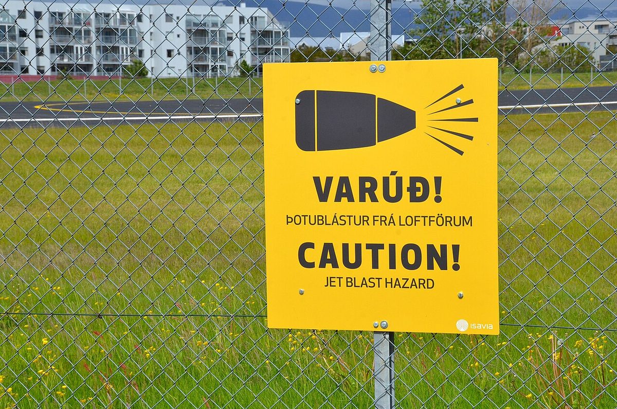 A warning sign at an airport perimeter cautioning against jet blast from departing aircraft.