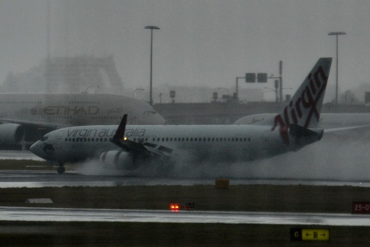 A jet airliner rolling out on a wet runway with spray thrown up behind its main wheels.