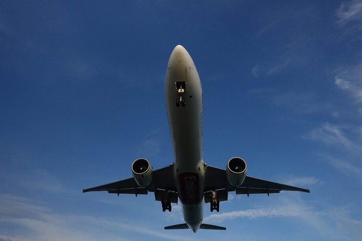A twin-engined airliner seen from below against a blue sky as it passes overhead to land, its wings angled back from the fuselage and narrowing towards the tips.