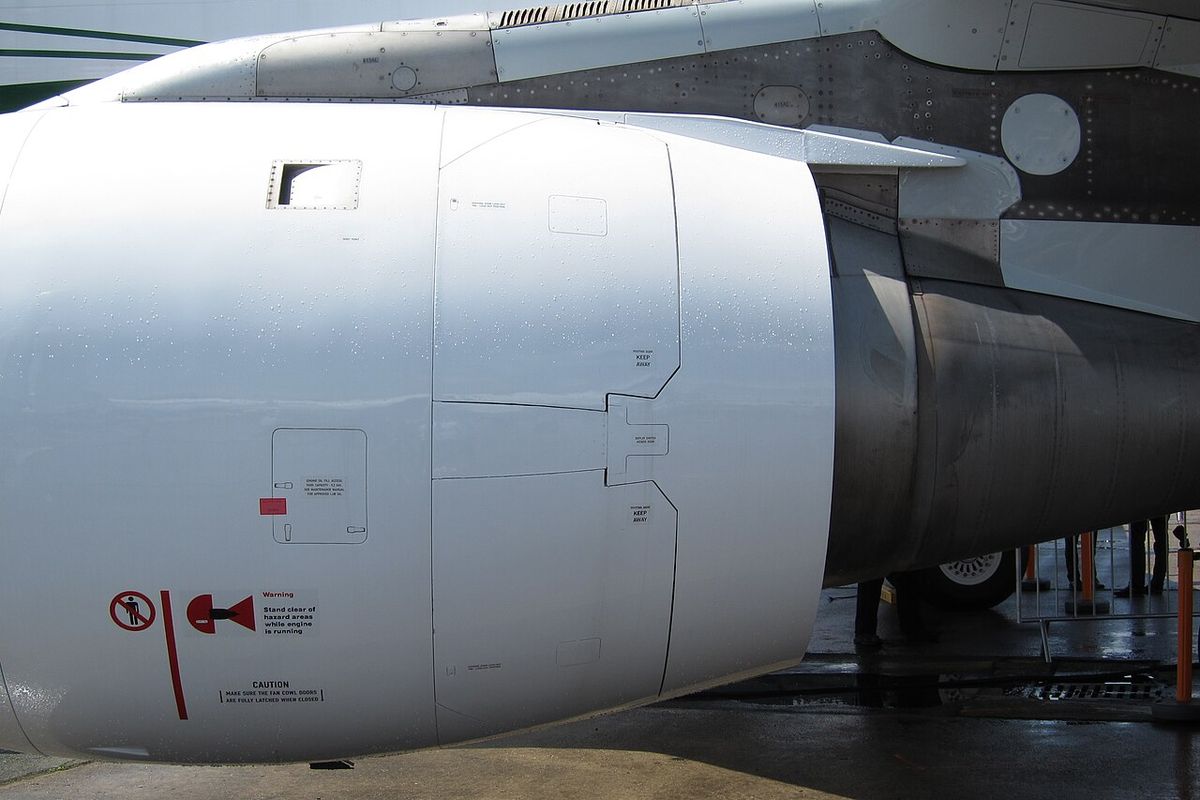 Side of a white jet engine nacelle under a wing, with the outlines of closed door panels in the rear half of the nacelle.