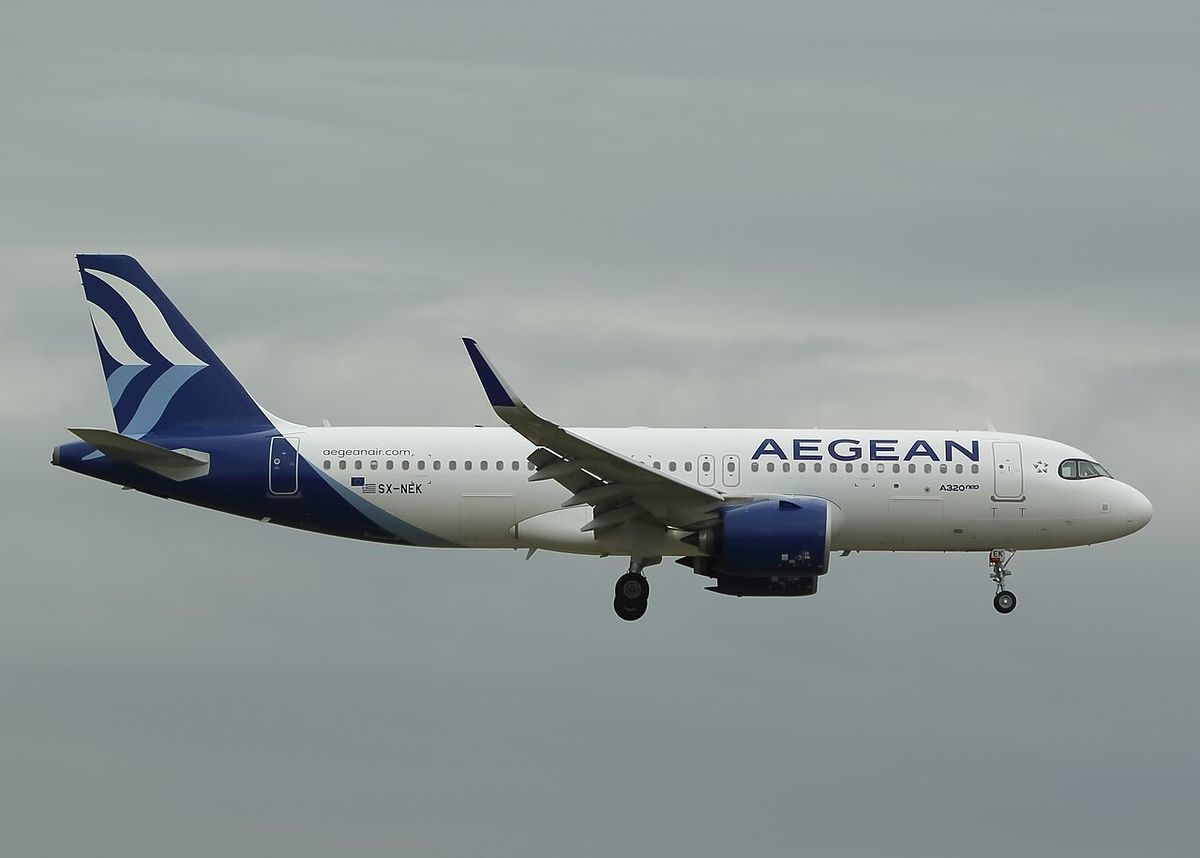 An Aegean Airlines Airbus A320neo in white and dark blue livery with the Aegean name on the fuselage, landing with its gear down against a gray sky.