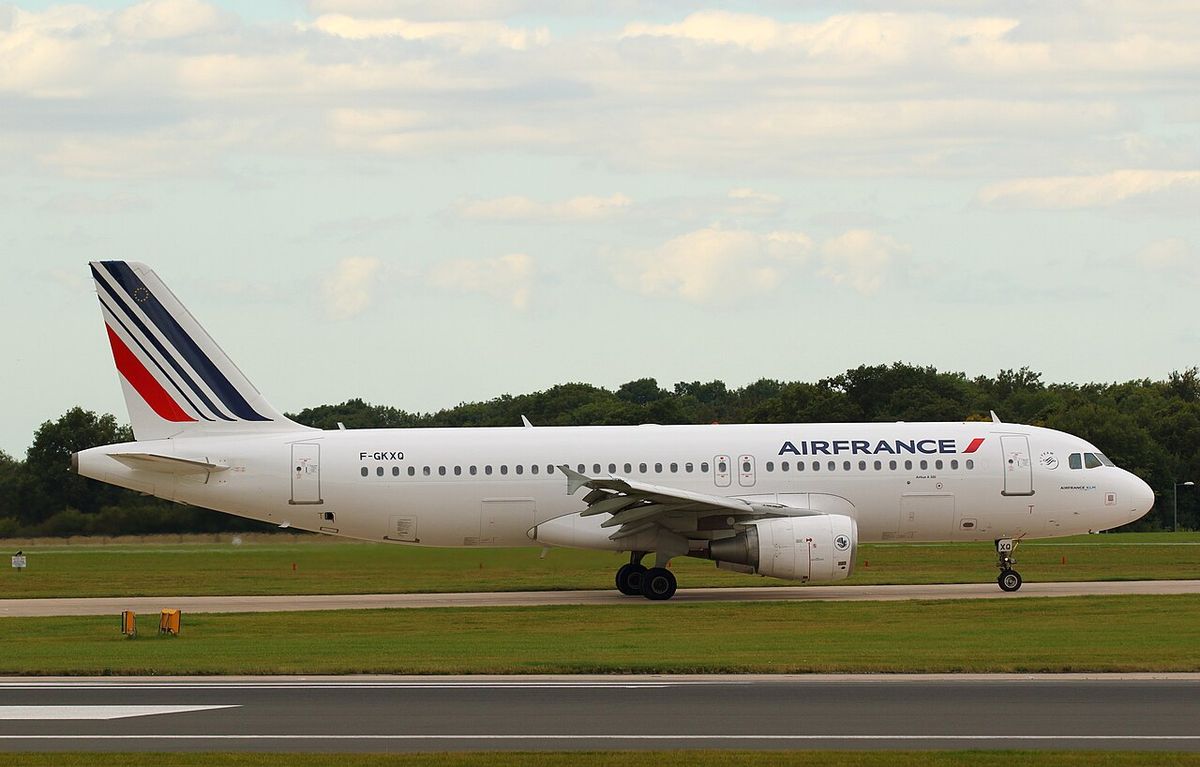 A white Air France Airbus A320 with a blue, white and red striped tail on a runway, trees behind.