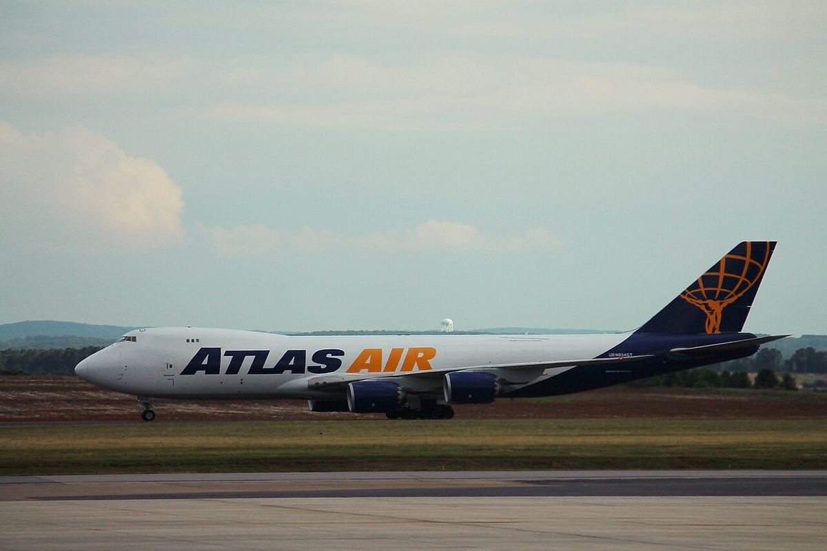 An Atlas Air Boeing 747-8F freighter in white livery with the blue Atlas Air titles and globe tail, taxiing past grass.