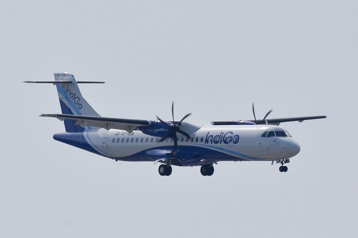 An IndiGo ATR 72-600 on final approach with its landing gear down, six-bladed propellers turning, against a pale gray sky.