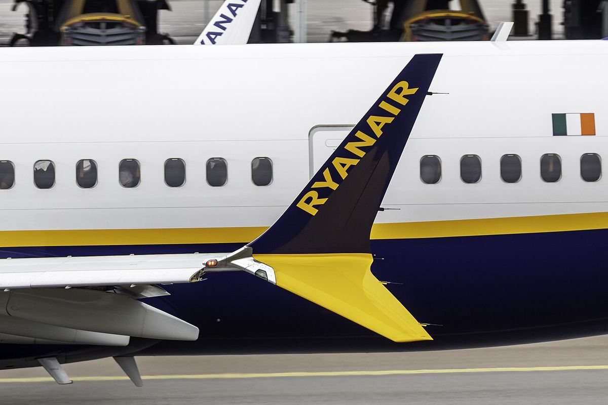 Dark blue upswept wingtip blade with yellow lettering and a shorter yellow blade pointing down, seen against the fuselage of a parked airliner.