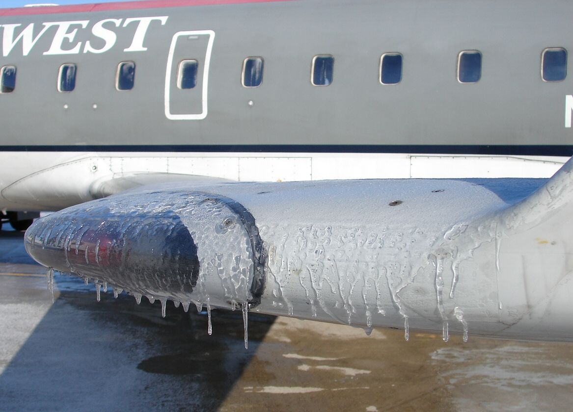 Thick, glassy, transparent ice with dripping icicles coating an aircraft wing.