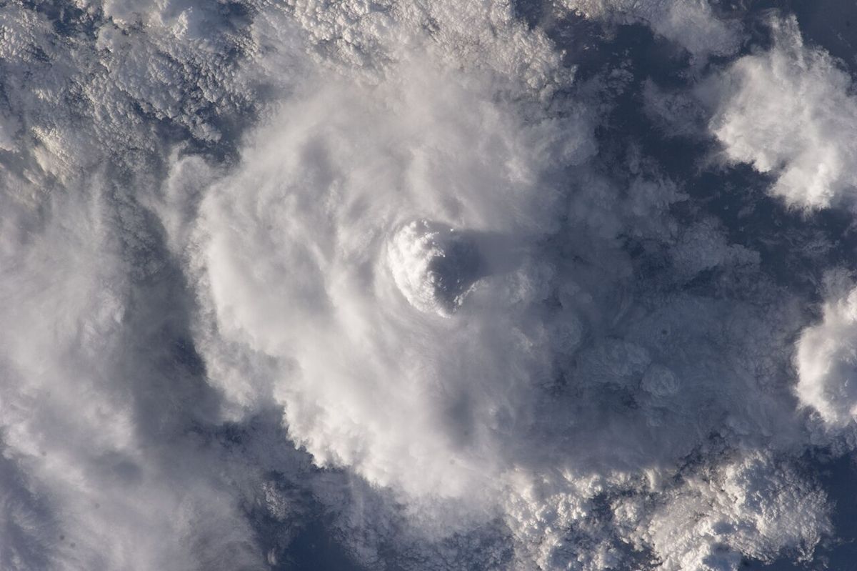 Seen from above, a round white anvil cloud spreading over lower clouds, with a bright dome bulging up at its centre and casting a shadow.
