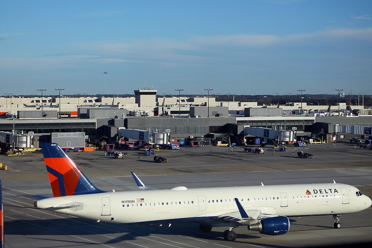 A white and dark blue Delta Airbus A321 with a red and blue tail on an apron, terminal buildings behind.