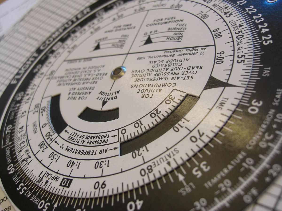 Close-up of the white circular slide rule of an E6B flight computer, with printed scales and windows for altitude and air temperature.