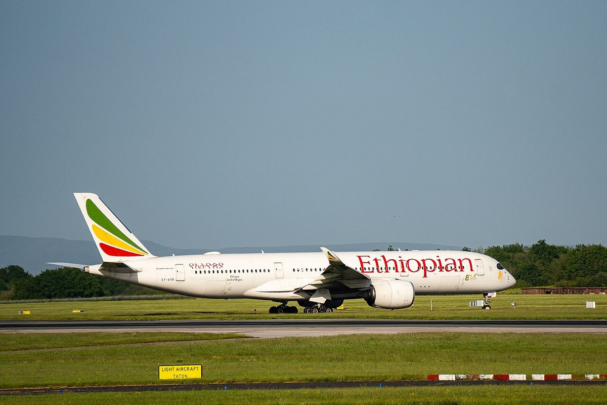A white Ethiopian Airlines Airbus A350 with a green, yellow and red tail rolling on a runway beside green grass.