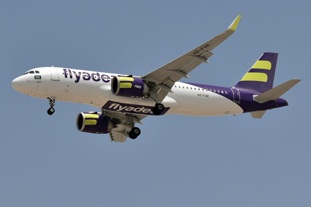 A flyadeal Airbus A320neo in its white and purple livery in flight with its landing gear down.