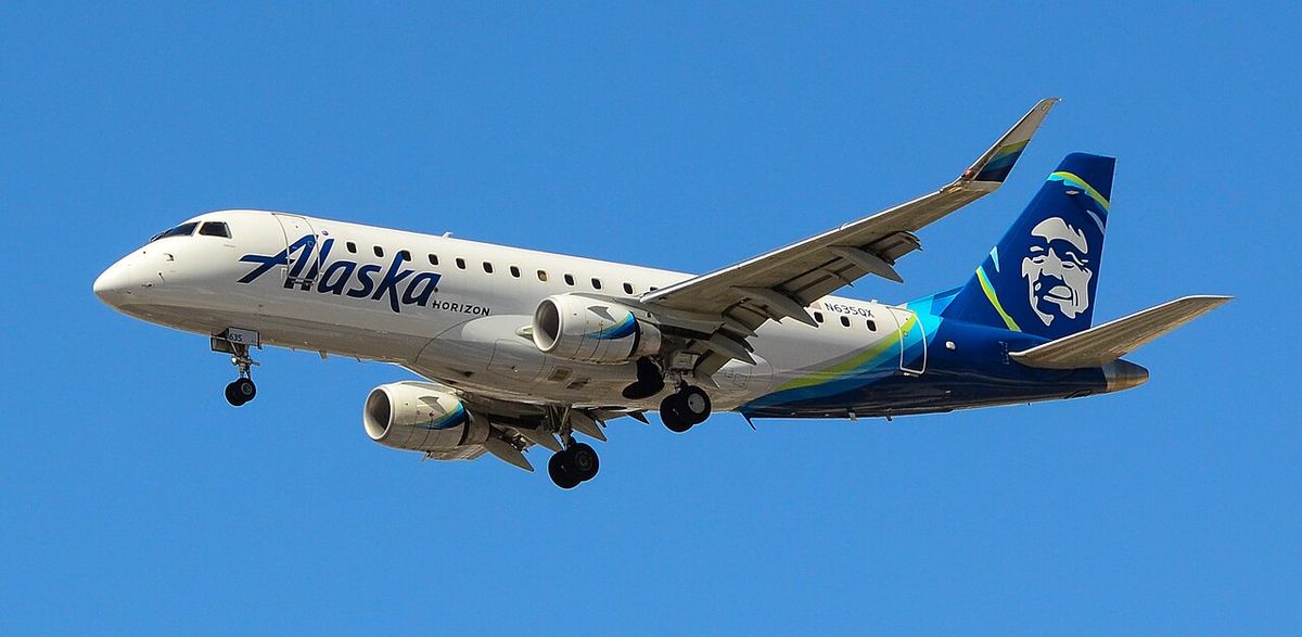 A Horizon Air Embraer 175 in Alaska Airlines colors in flight with its landing gear down.