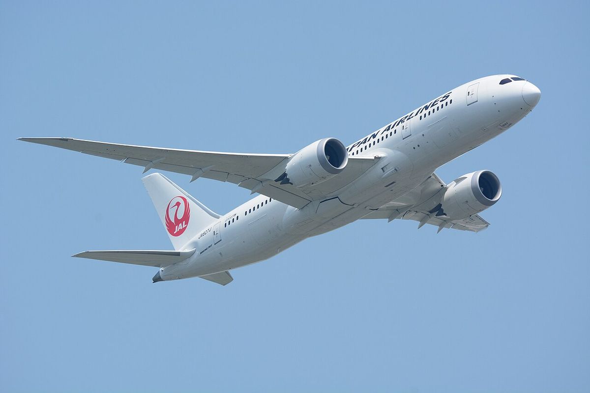A Japan Airlines Boeing 787-8 in white livery with the red crane logo on the tail, climbing with the gear up.