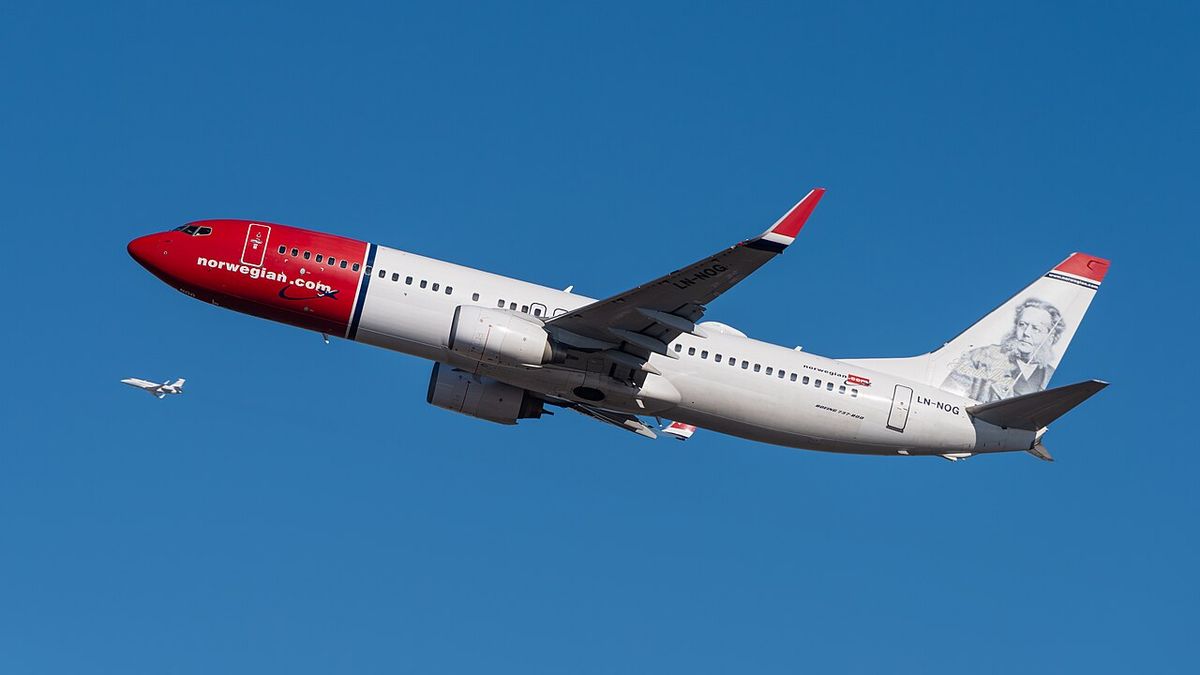 A white Boeing 737 with a red nose and a portrait on its tail climbing away against a deep blue sky, landing gear up.