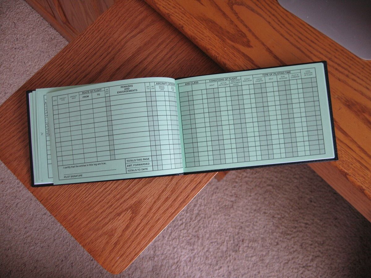 An open logbook on a wooden table, its two pages ruled into many narrow columns and rows.