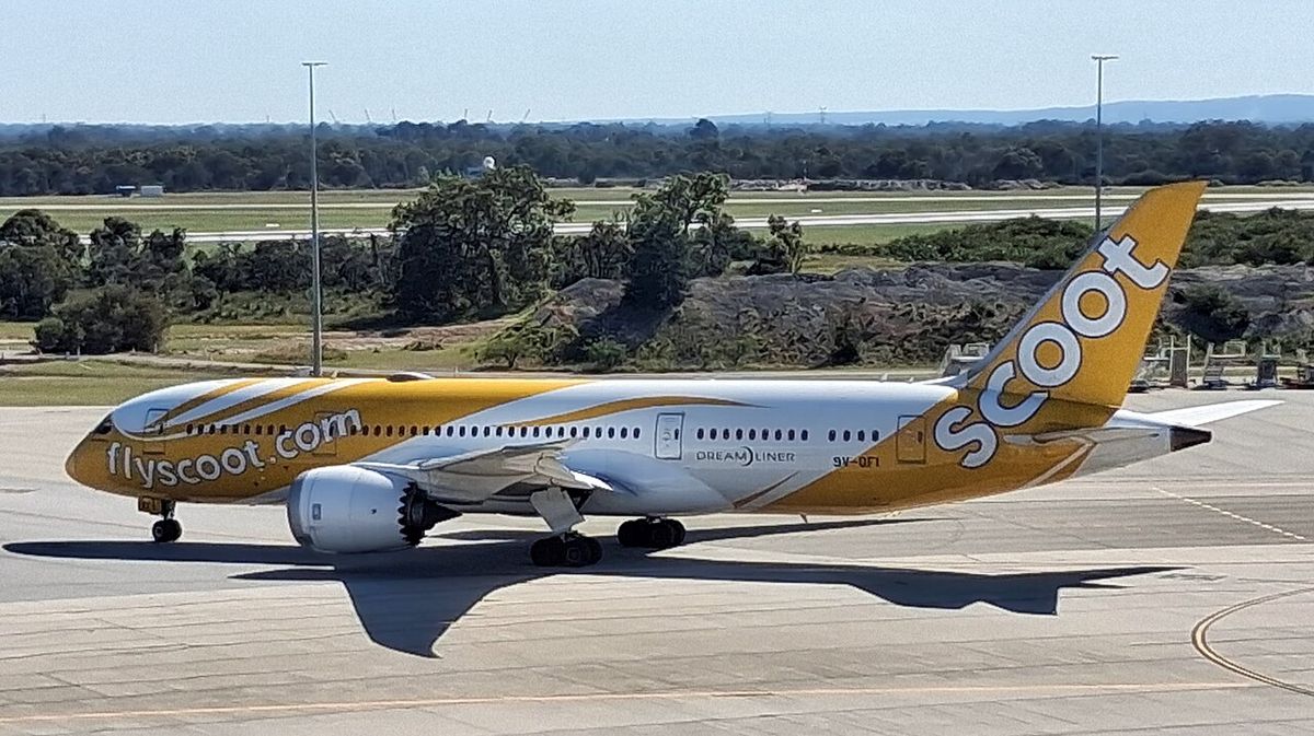 A Scoot Boeing 787 in its yellow and white livery taxiing on an airport apron.