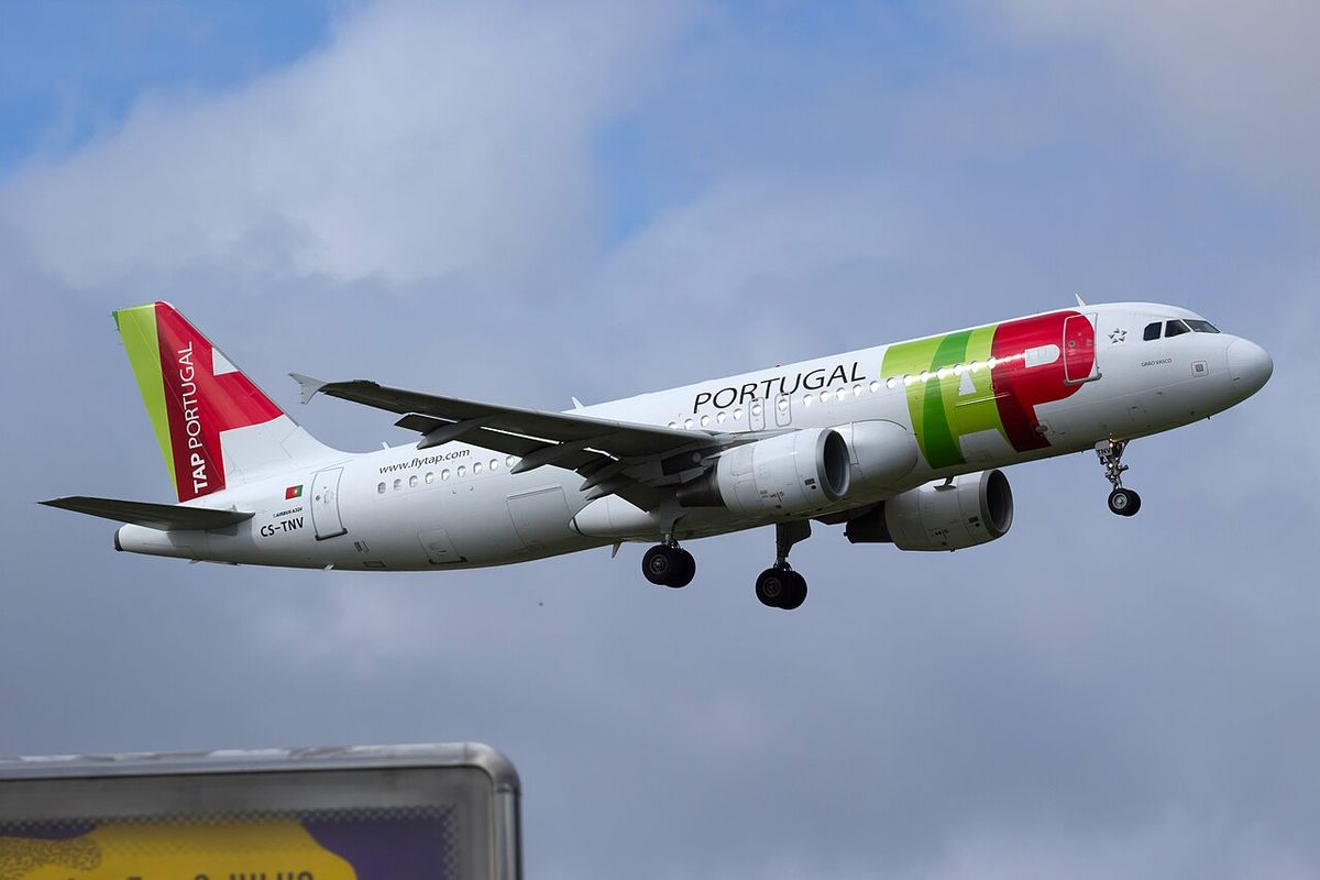 A white TAP Airbus A320 with a green and red logo near the nose and a red and green tail, landing gear down, under cloud.
