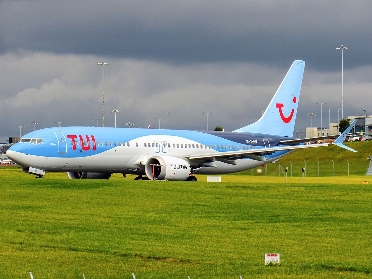 A TUI Boeing 737 MAX 8 in light blue livery with the red TUI logo on the tail, taxiing past grass at an airport.