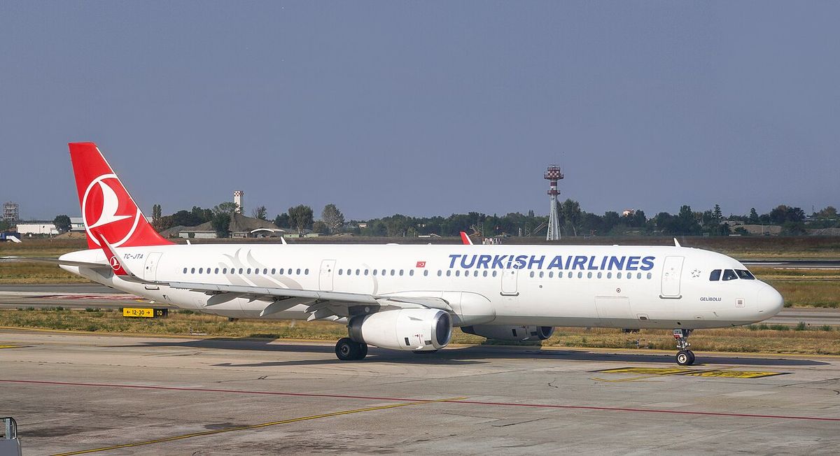 A white Turkish Airlines Airbus A321 with a red tail taxiing on an airport apron.