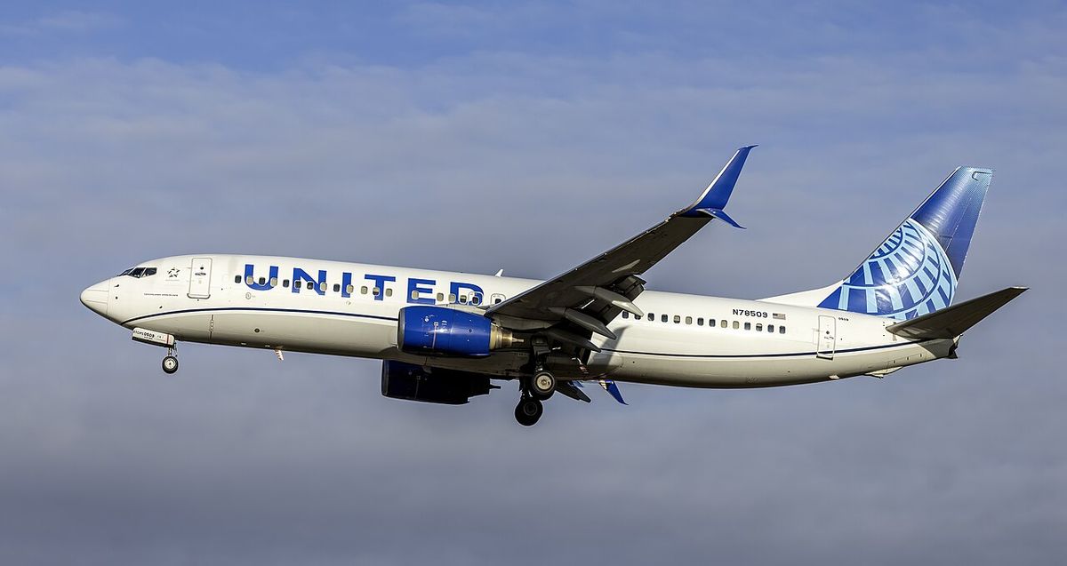 A white United Airlines Boeing 737 with a blue belly and a blue globe on its tail, landing gear down, under cloud.