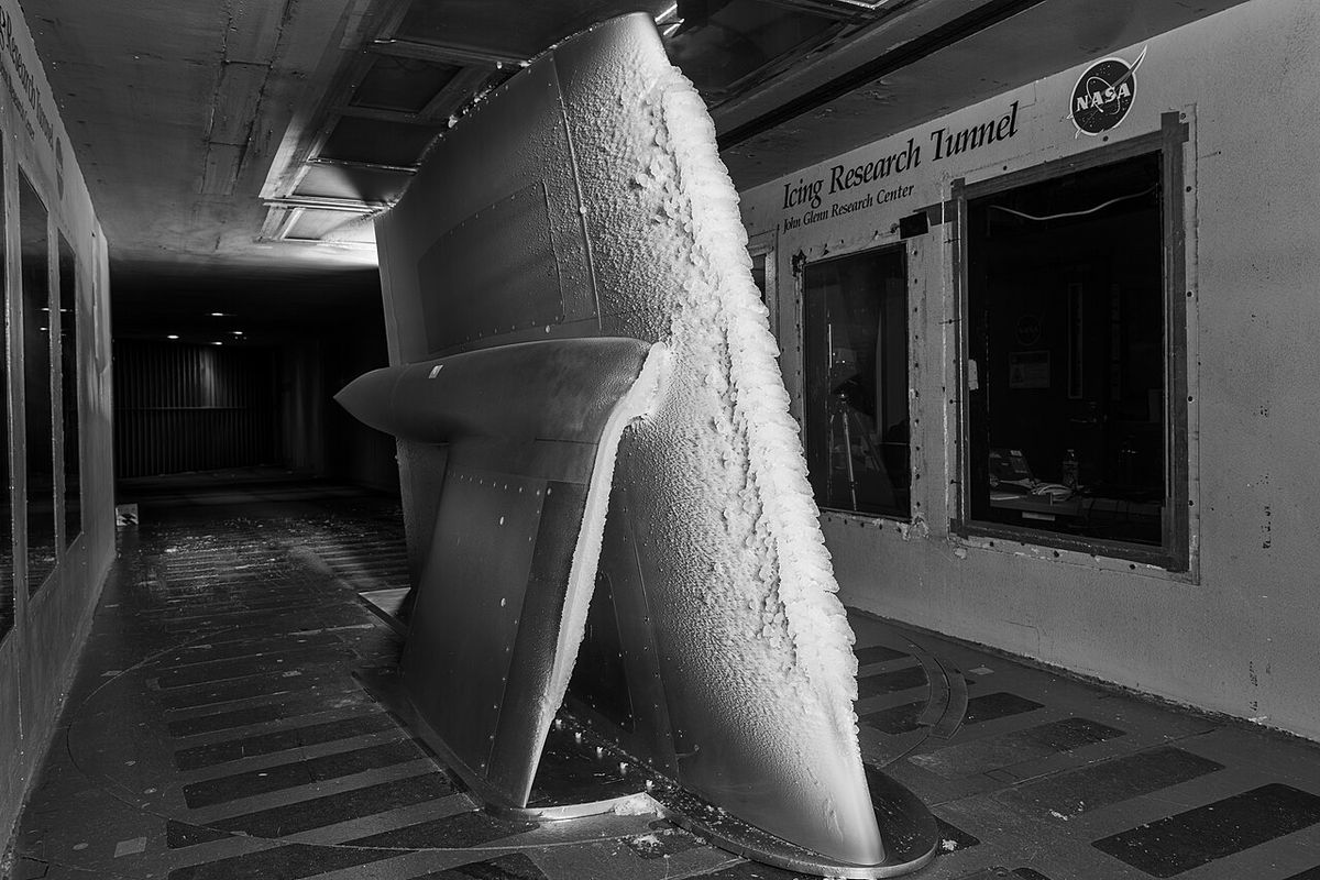 A large wing model standing upright in a wind tunnel, its leading edge coated with a thick, rough band of white ice.